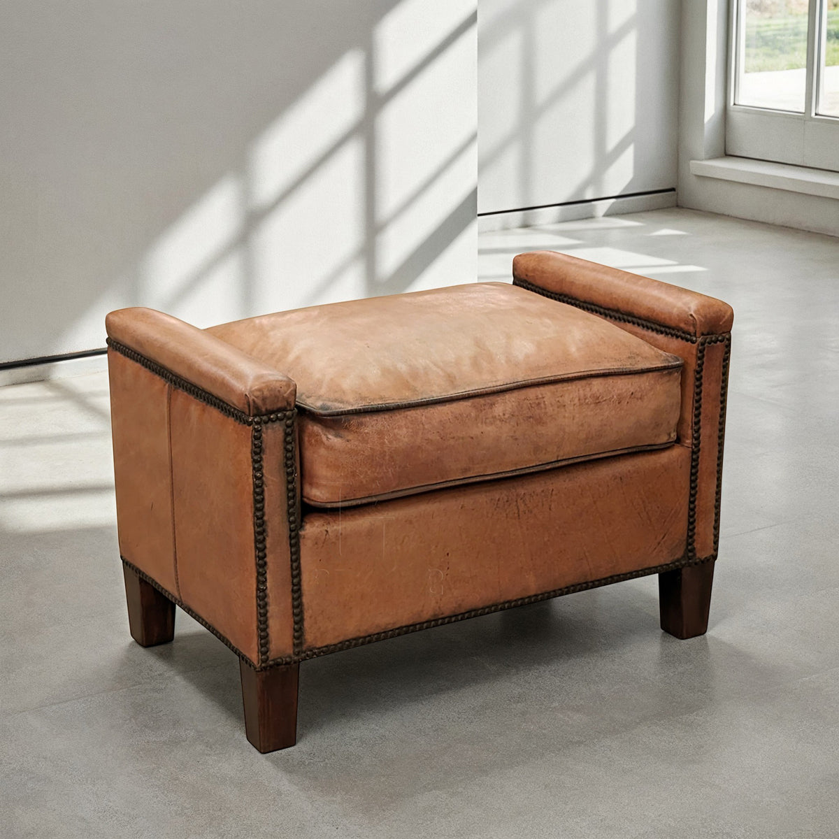Leather ottoman with squared wood legs and nailhead trim.