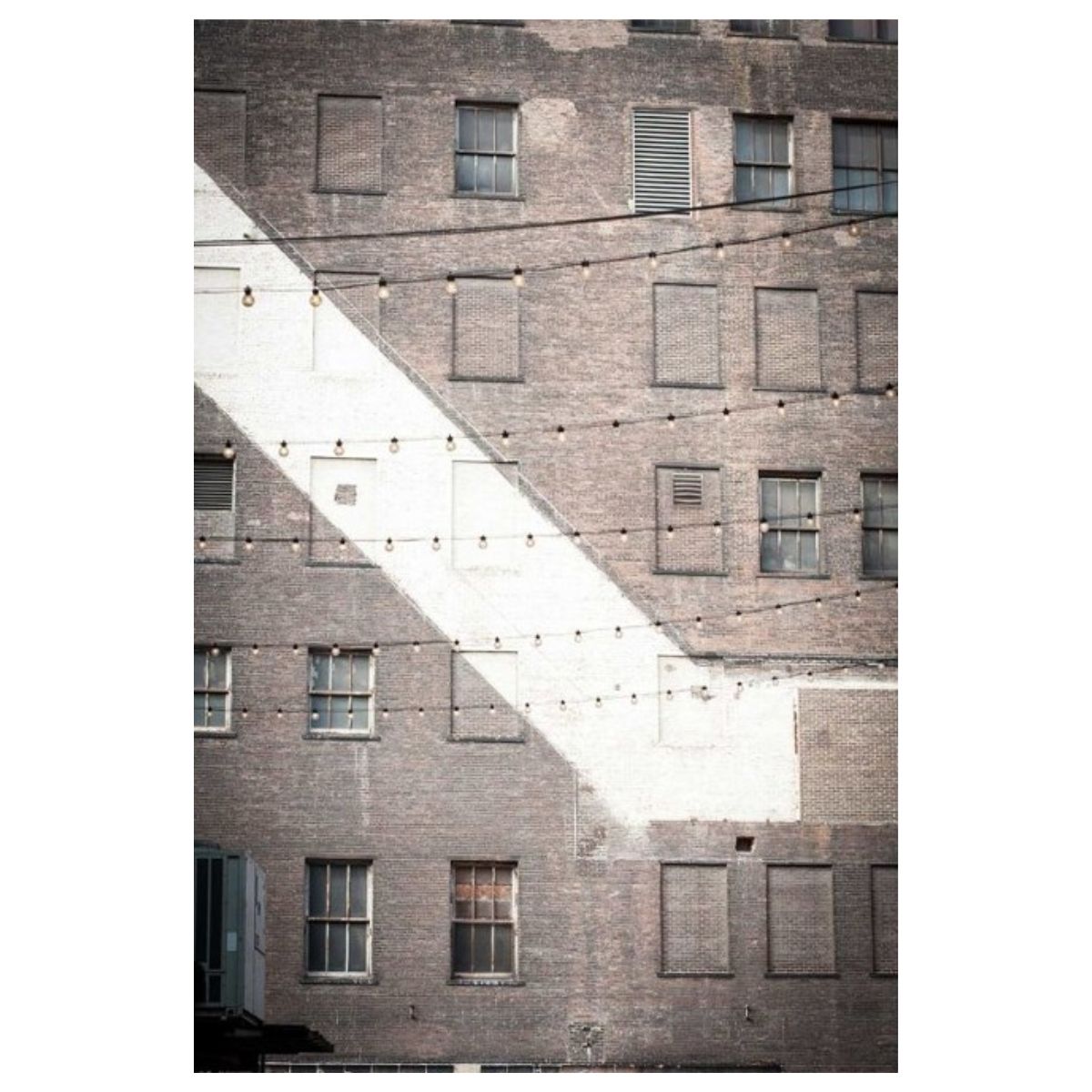 Photograph of a weathered brick facade with windows and string lights