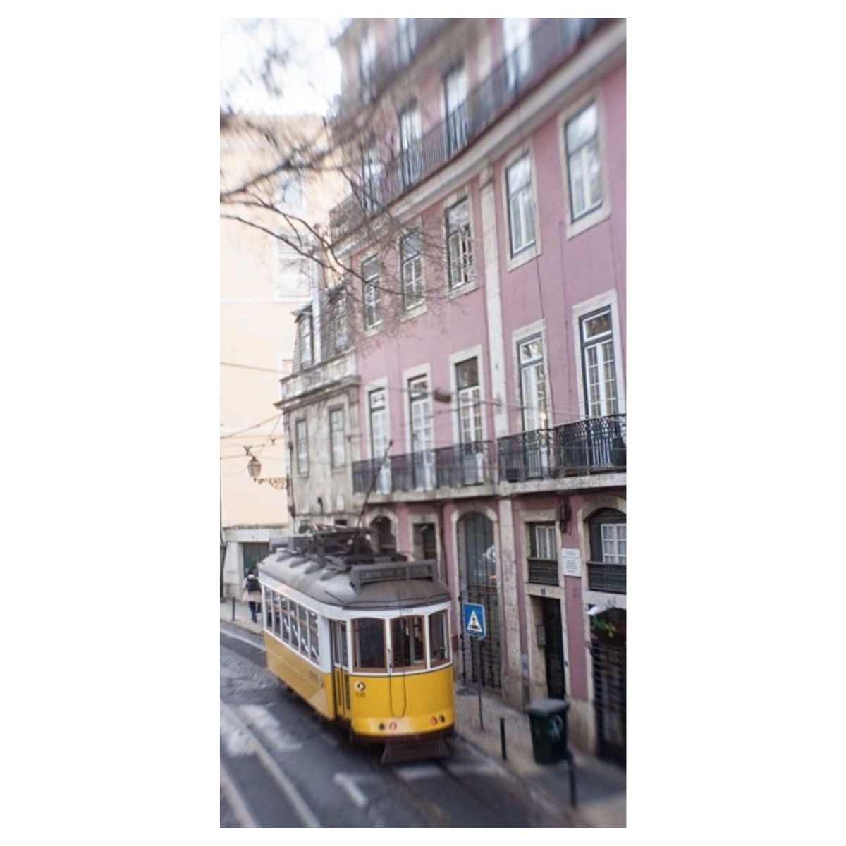Photograph of a yellow Lisbon tram passing pastel building facades